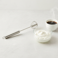 Stainless steel rotary whisk beside whipped cream and coffee