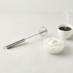 Stainless steel rotary whisk beside whipped cream and coffee