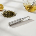 Stainless steel tea infuser beside loose tea leaves and a glass teapot